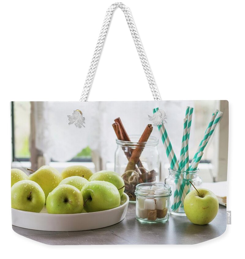 Ip_11339398 Weekender Tote Bag featuring the photograph Green Apples, Sugar Cubes And Cinnamon Sticks On A Kitchen Table by Natasha Breen