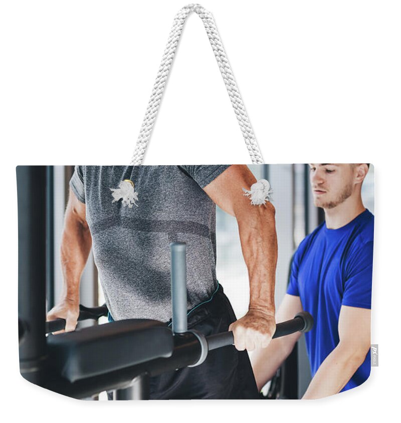 Man Weekender Tote Bag featuring the photograph Gym instructor helping senior man at the gym. by Michal Bednarek