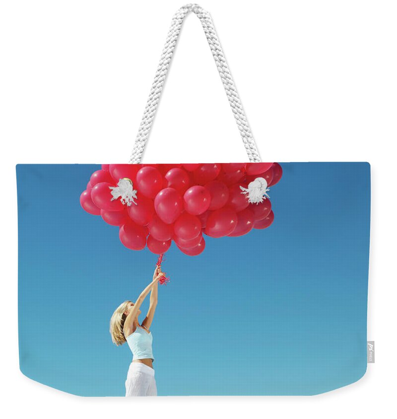 Hand Raised Weekender Tote Bag featuring the photograph Young Woman Holding On To Large Bunch by Nick Dolding
