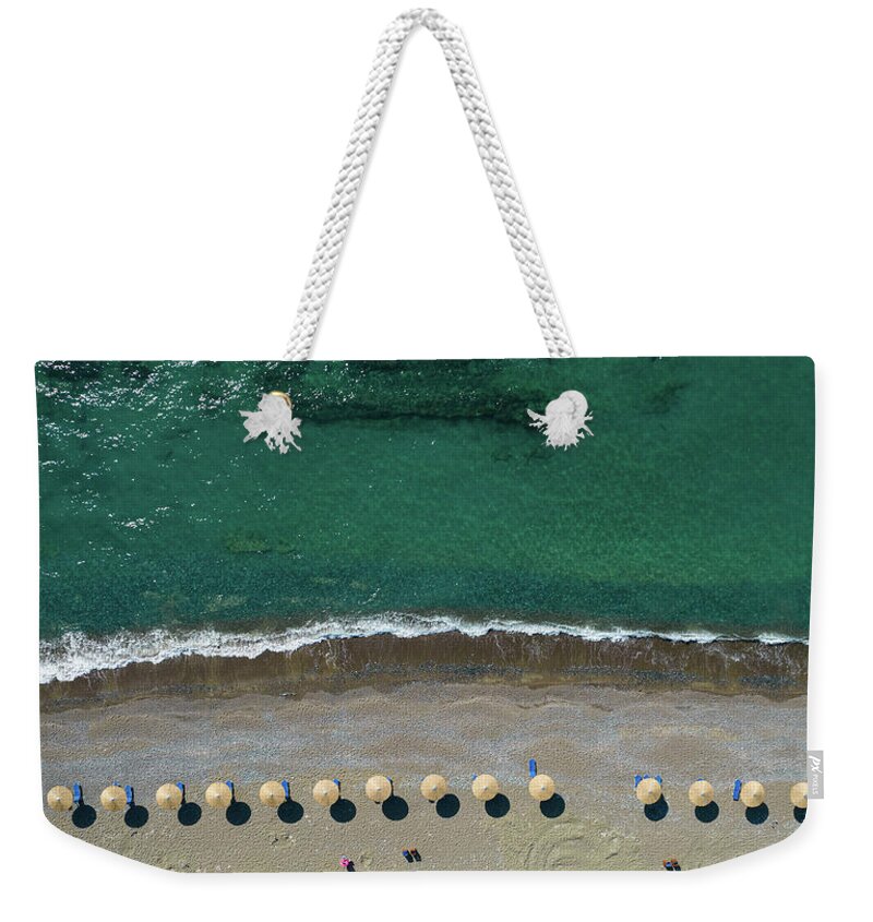 Summertime Weekender Tote Bag featuring the photograph Aerial view from a flying drone of beach umbrellas in a row on an empty beach with braking waves. by Michalakis Ppalis
