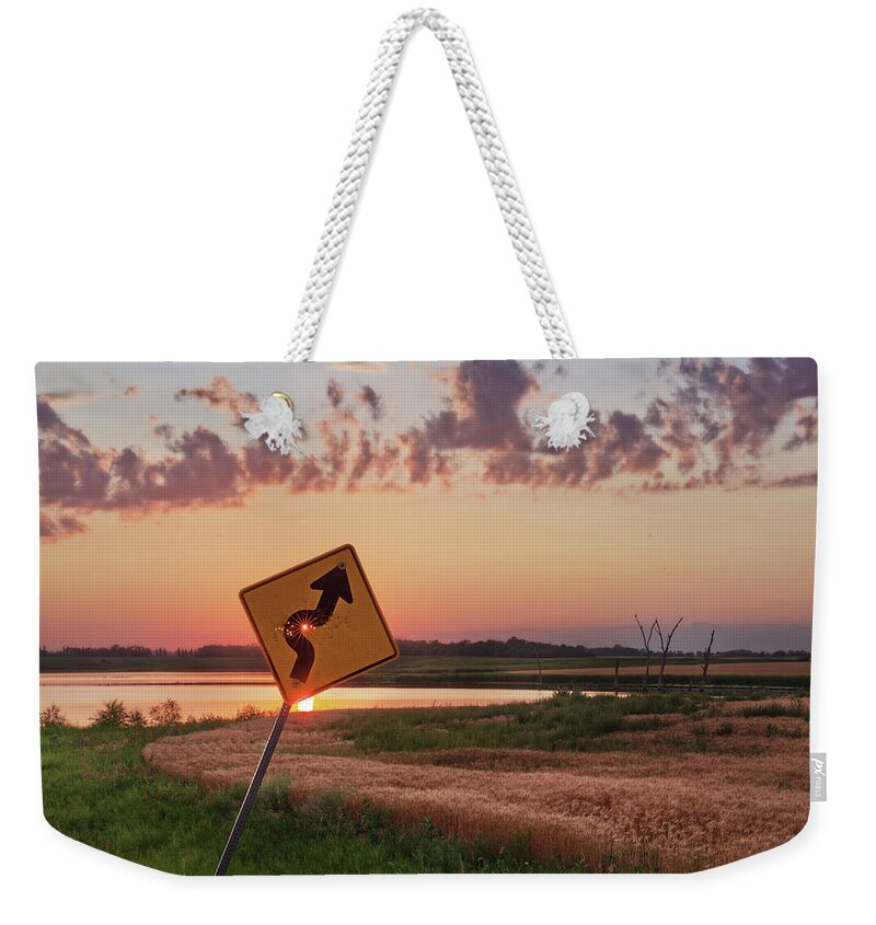 Sign Curve Scenic Landscape North Dakota Lake Syzygy Alignment Sun Pinhole Roadsign Hunting Bullet Humor Star Bullet Hole Shooting Shot Weekender Tote Bag featuring the photograph Dodged a Bullet - curve in road sign with sunlight through bullet hole by Peter Herman