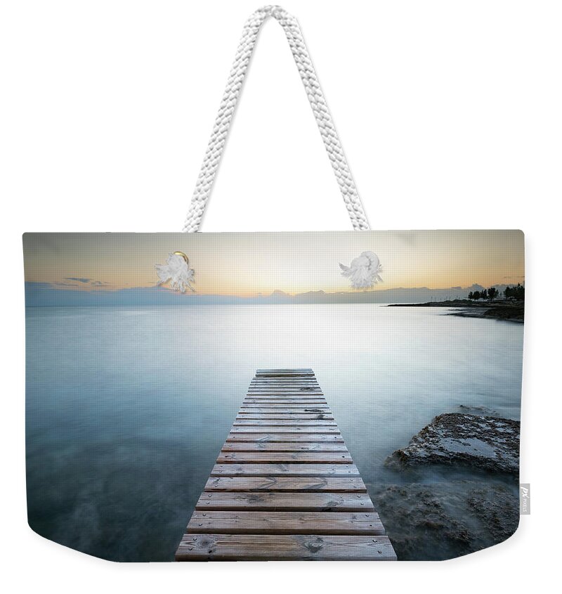 Tranquil Weekender Tote Bag featuring the photograph Long wooden pier in the sea at sunrise. #1 by Michalakis Ppalis