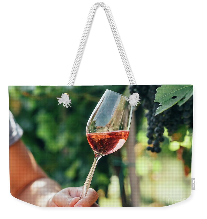 Wine Weekender Tote Bag featuring the photograph Man holding glass of red wine in vineyard field. Wine tasting in #1 by Jelena Jovanovic