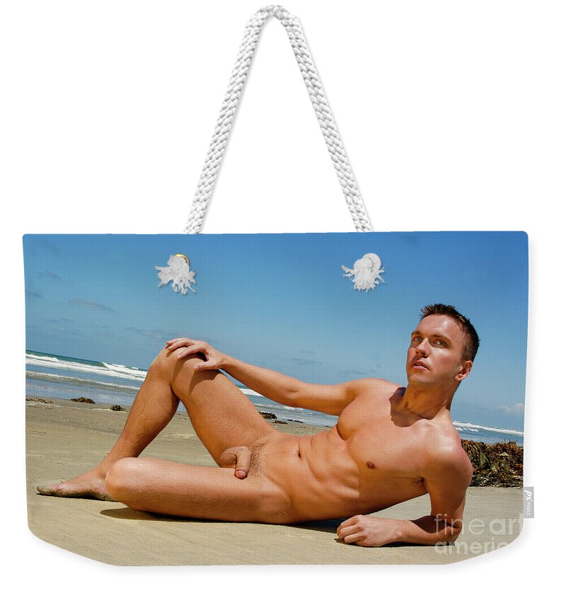 Nude Weekender Tote Bag featuring the photograph Handsome nude and muscular man poses on the wet sand at the beach. by Gunther Allen