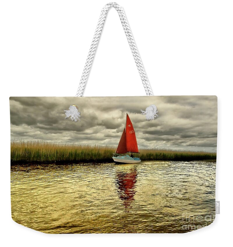 Red Blue Gold Yellow Sail Water Sailor Sailing Calm Beautiful Lake River Reeds Happy Joy Joyful Solo Single Alone Relaxing Romantic Atmospheric Solitude Clouds Colorful Color Boat Reflections Serene Solitary Tranquil Tranquillity Elements Vibrant Timeless Still Calmness Peaceful Breathtaking Mind-blowing Nature Bright Vivid Golden Patterns Surf Way Charming Relaxation Painterly Magical Sunset Dawn Delightful Serenity Cheerful Jolly Awesome Allure Seascape Simplicity Minimalism Loneliness Poetic Weekender Tote Bag featuring the photograph Hundred shades of GOLD - RED SAIL IN GOLD WATERS by Tatiana Bogracheva