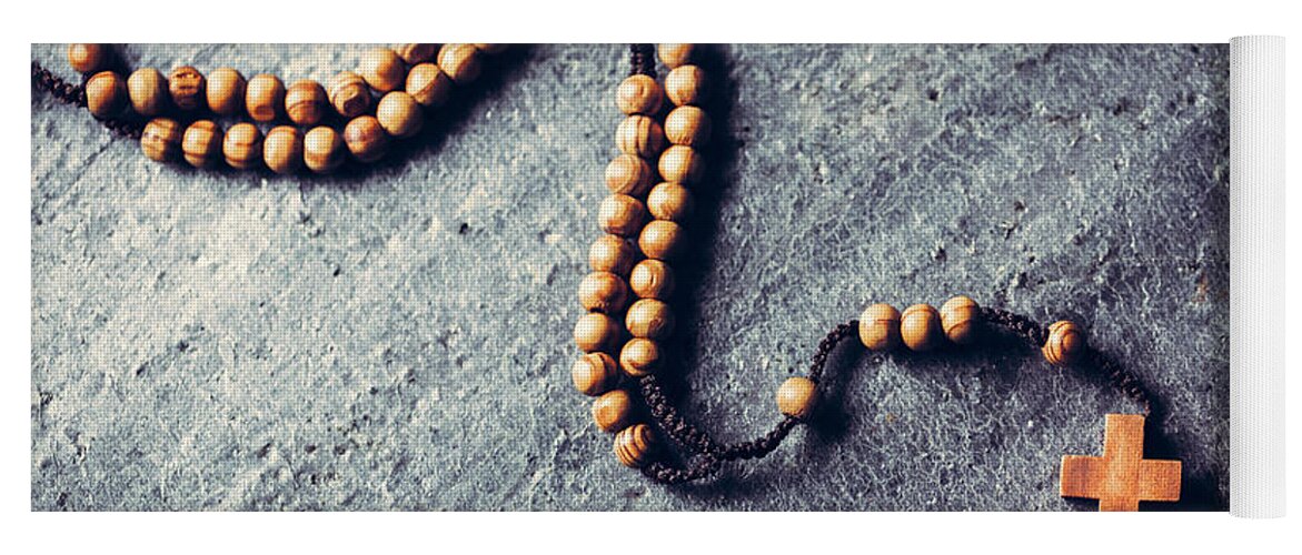 Cross Yoga Mat featuring the photograph Wooden rosary laying on stone background. by Michal Bednarek