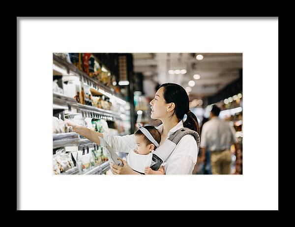 Toddler Framed Print featuring the photograph Beautiful Asian woman carrying cute baby girl shopping for organic green marketing products in grocery store by D3sign