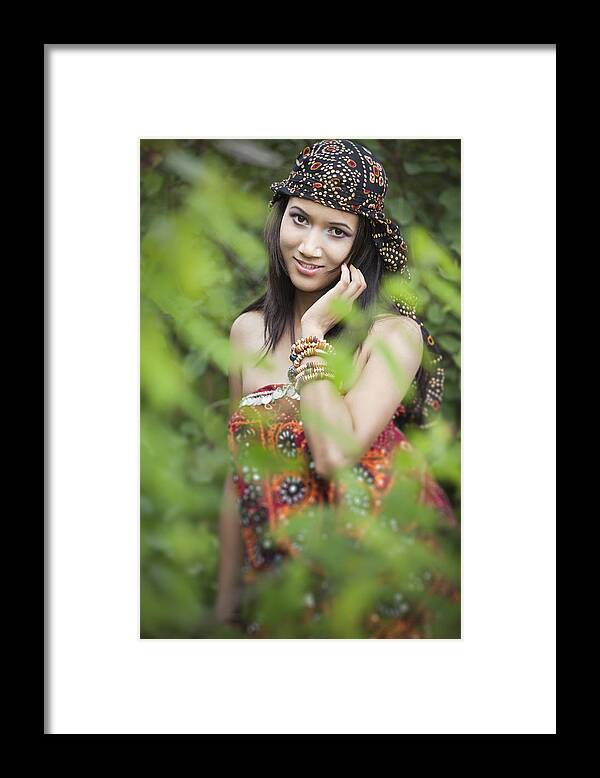 Asian And Indian Ethnicities Framed Print featuring the photograph Beautiful young woman in nature behind foliage. by Gawrav
