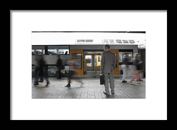 Young Men Framed Print featuring the photograph Commuters passing businessman on platform, (blurred motion) by Toby Burrows