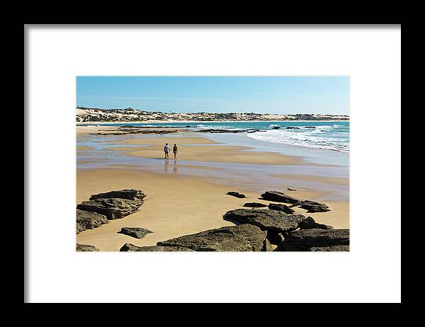 Water's Edge Framed Print featuring the photograph Couple Walking On Empty Beach In by John Seaton Callahan