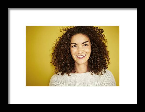 Tranquility Framed Print featuring the photograph Curly haired mixed race woman smiling openly at camera on vibrant yellow backdrop by Justin Lambert