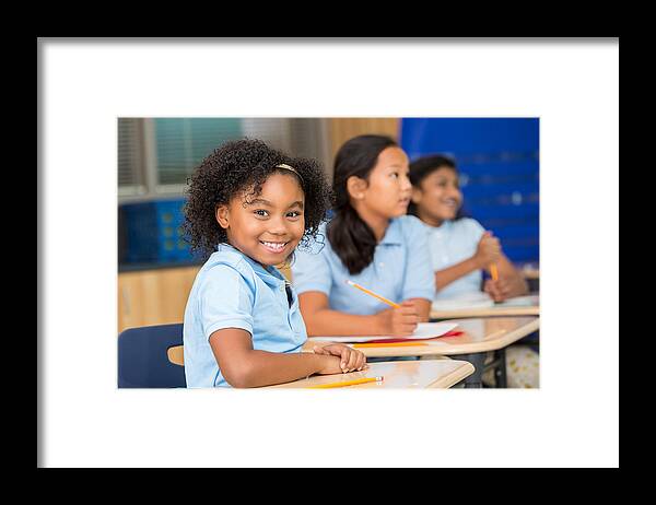 Asian And Indian Ethnicities Framed Print featuring the photograph Cute schoolgirl smiles at the camera in classroom by SDI Productions