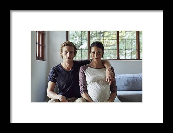 Heterosexual Couple Framed Print featuring the photograph Expectant couple sitting on sofa at home by Morsa Images
