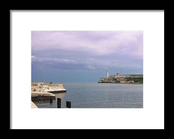 Water's Edge Framed Print featuring the photograph Havana Malecon with Morro lighthouse and a lonely, unrecognizable person relaxing by the sea, Cuba by Smartshots International
