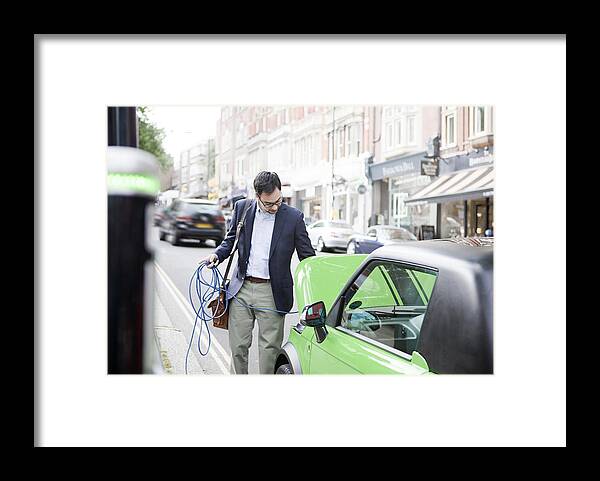 Young Men Framed Print featuring the photograph Man charging electric car on street by Nancy Honey