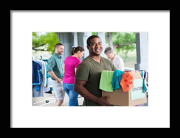 Young Men Framed Print featuring the photograph Man holding box of clothes donations at a donation center by SDI Productions