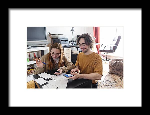 Young Men Framed Print featuring the photograph Millennial couple using digital payment to share expense. by Martinedoucet