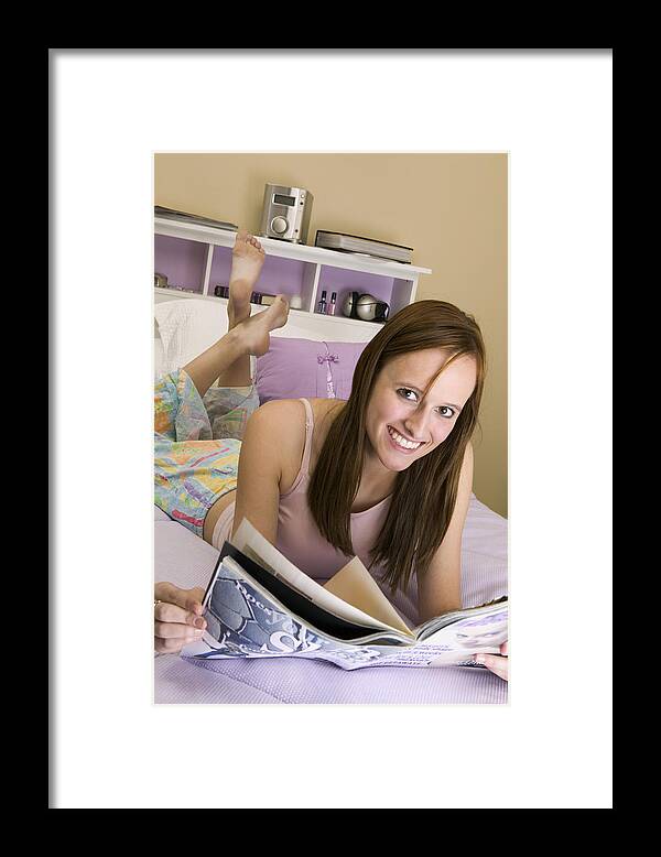 Casual Clothing Framed Print featuring the photograph Portrait of a teenage girl lying on a bed holding a magazine by Photodisc