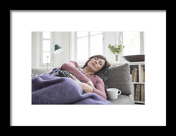 Mature Adult Framed Print featuring the photograph Woman with stomach ache lying on the sofa by Westend61