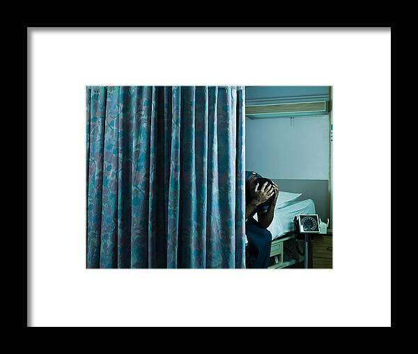 Young Men Framed Print featuring the photograph Young male doctor sitting on hospital bed with head in hands by Image Source