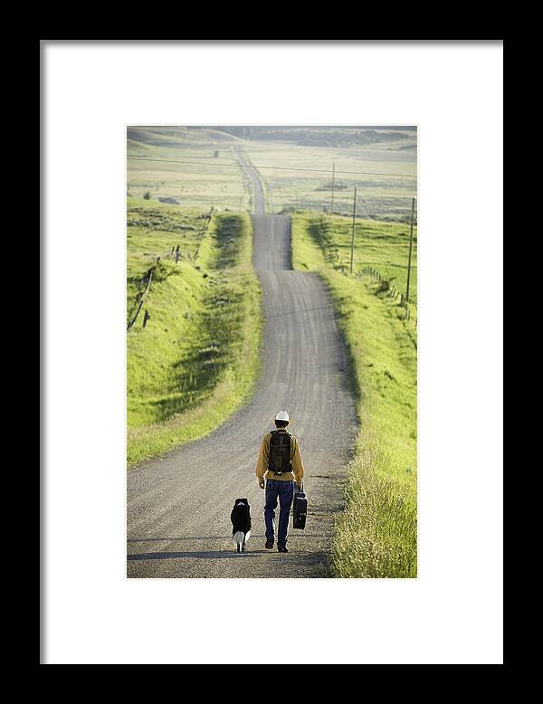 Pets Framed Print featuring the photograph Young man walking with dog down rural road, rear view by Zia Soleil