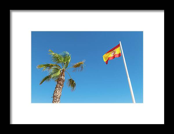 Spain Framed Print featuring the photograph Spanish flag and palm tree in the blue sky by GoodMood Art