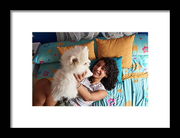 Girl Framed Print featuring the photograph A Little Girl Is Playing With Her White Pomeranian Puppy In Bed. by Cavan Images