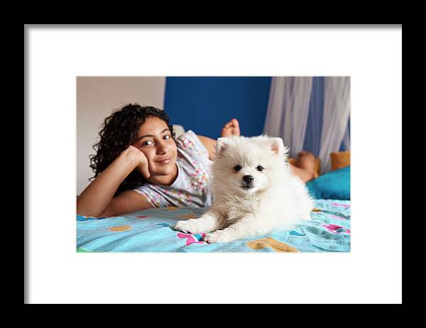 Girl Framed Print featuring the photograph A White Pomeranian Puppy Looks At The Camera In The Foreground by Cavan Images