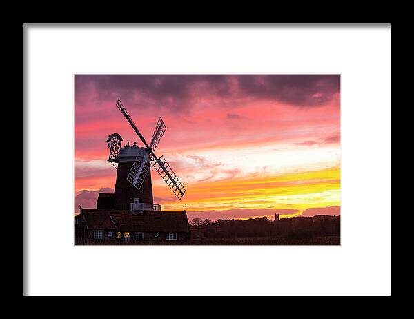 Windmill Framed Print featuring the photograph A Windmill At Cley Next The Sea, North Norfolk, Uk, With Blakeney Church In The Background At Sunset. by Cavan Images