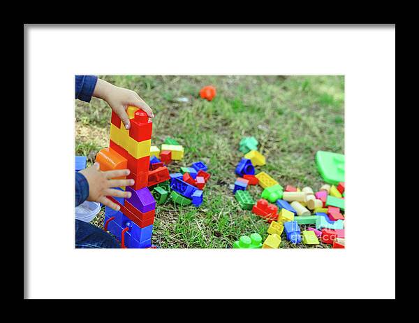 Activity Framed Print featuring the photograph Child playing with colorful blocks sitting on the ground of a garden in spring, negative space. by Joaquin Corbalan