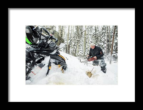 Motorsports Framed Print featuring the photograph Retired Elderly Man Using Chainsaw To Clear Trails While Snowmobiling. by Cavan Images