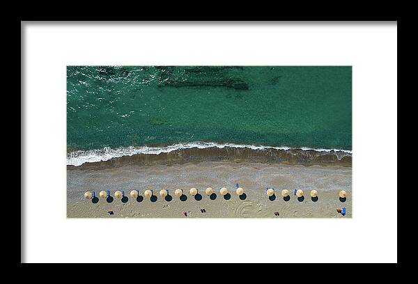 Summertime Framed Print featuring the photograph Aerial view from a flying drone of beach umbrellas in a row on an empty beach with braking waves. by Michalakis Ppalis