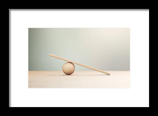 Risk Framed Print featuring the photograph Wooden Seesaw Scale Sitting on Wood Surface in Front of Defocused Background by MicroStockHub