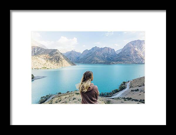 People Framed Print featuring the photograph Young woman looks out across mountain lake #1 by Andrii Lutsyk/ Ascent Xmedia
