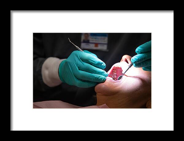 Human Mouth Framed Print featuring the photograph A Dentist Wearing Surgical Gloves Uses a Loupe Light to Examine the Teeth of a Female Patient in Her Sixties in a Dental Clinic by Hoptocopter