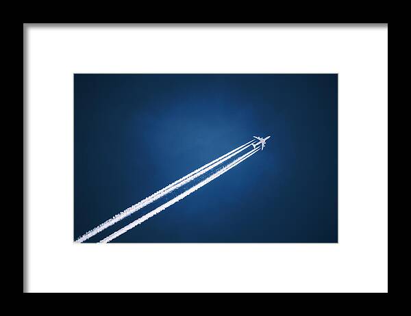 Mid-air Framed Print featuring the photograph A jet vapour trail across a dark blue sky. by Mint Images
