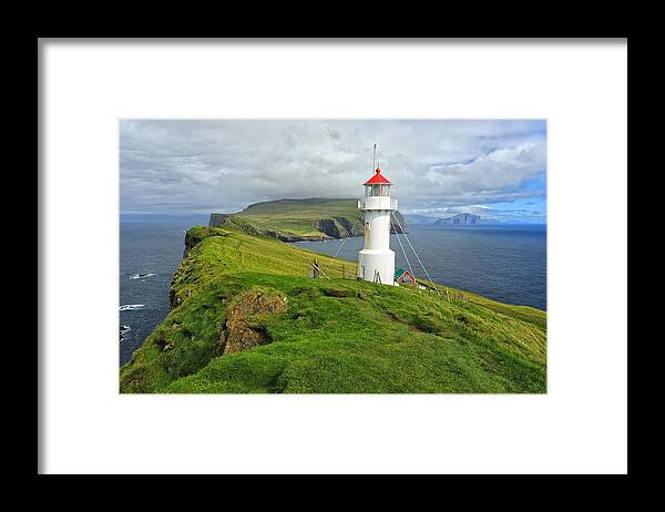 Scenics Framed Print featuring the photograph A small white lighthouse wit a red roof on top of grassy cliffs of Mykines Island by Rainer Grosskopf