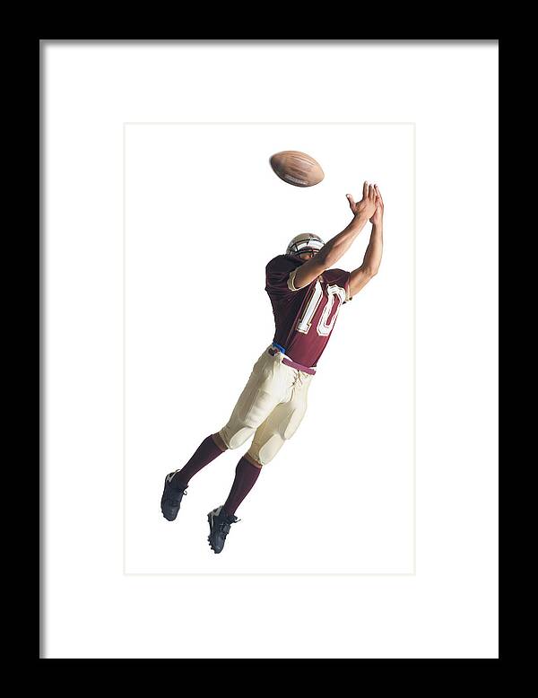 American Football Uniform Framed Print featuring the photograph An African American Football Player In A Red And White Uniform Is Jumping Up With Arms Outstretched To Catch A Football by Photodisc