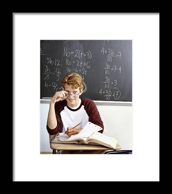 Working Framed Print featuring the photograph An Intelligent Looking Student Working at a Desk in a Classroom, with a Blackboard Behind him Covered in Algebra Equations by Digital Vision.