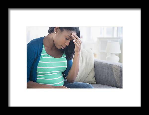 Problems Framed Print featuring the photograph Anxious Black pregnant woman rubbing forehead on sofa by JGI/Jamie Grill