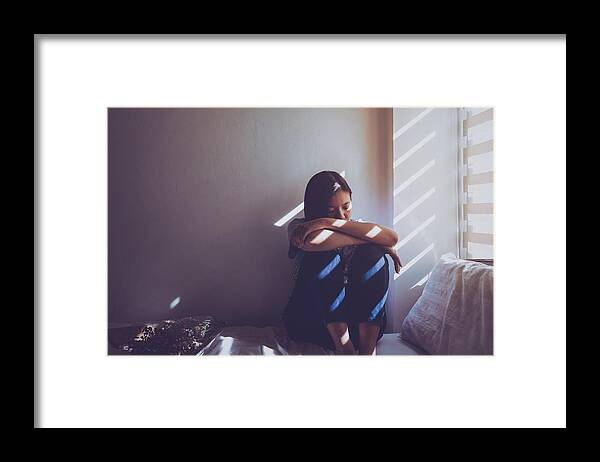 Problems Framed Print featuring the photograph Asian women are sitting hugging their knees in bed. Feeling sad, disappointed in love In the dark bedroom and sunlight from the window through the blinds.Vintage tone. by Bunditinay