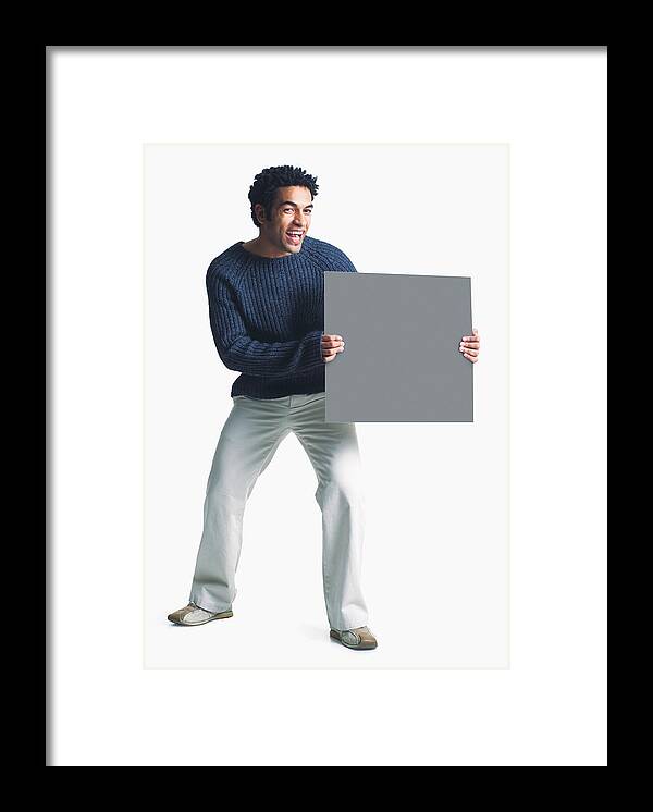 White Background Framed Print featuring the photograph Attractive African American Man Wears Khaki Pants Grey Sweater Holds Blank Sign Smiles Enthusiasm by Photodisc