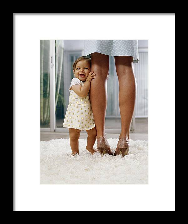 Rug Framed Print featuring the photograph Baby girl (6-9 months) standing on rug, holding onto mother's legs by Kraig Scarbinsky