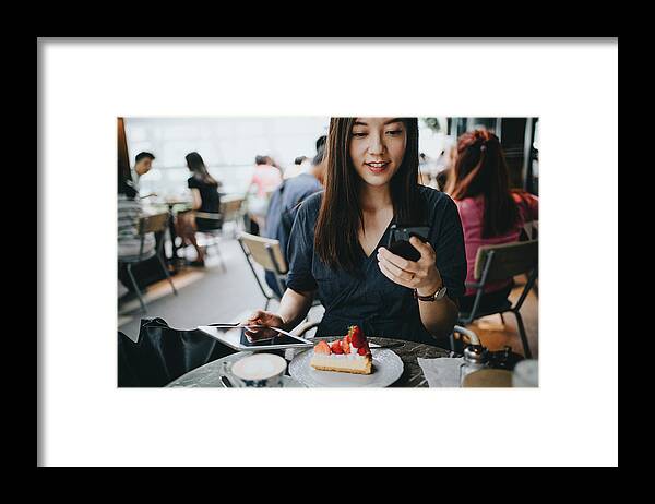 Expertise Framed Print featuring the photograph Busy young woman using smartphone while working on digital tablet in an outdoor cafe by D3sign