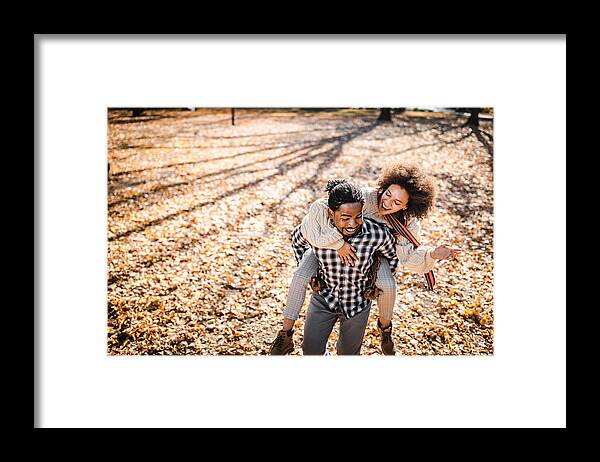 Young Men Framed Print featuring the photograph Cheerful African American couple piggybacking in autumn at the park. by Skynesher