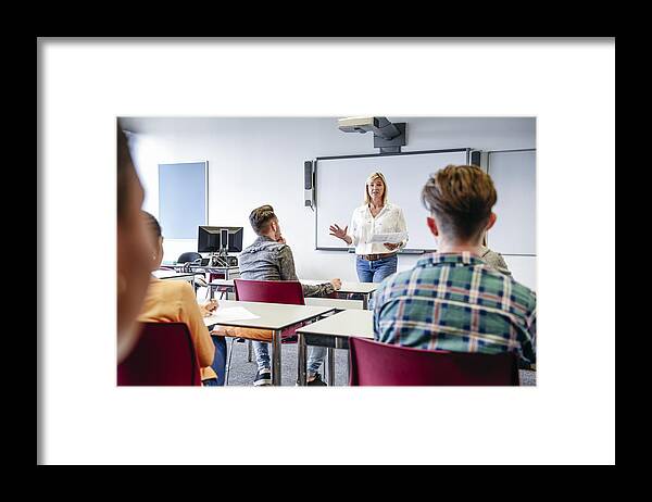 Young Men Framed Print featuring the photograph College lecturer in classroom with students sitting at desks, listening by JohnnyGreig