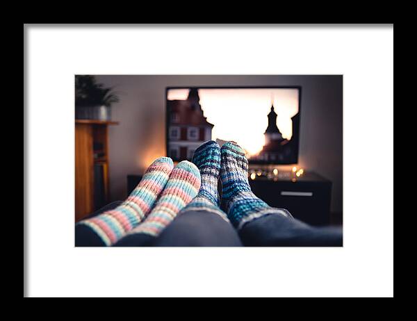 Tranquility Framed Print featuring the photograph Couple with socks and woolen stockings watching movies or series on tv in winter. Woman and man sitting or lying together on sofa couch in home living room using online streaming service. by Tero Vesalainen
