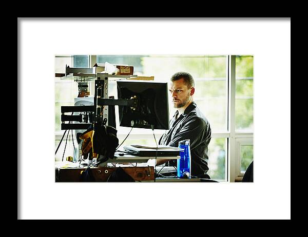 Expertise Framed Print featuring the photograph Engineer standing at desk designing project by Thomas Barwick