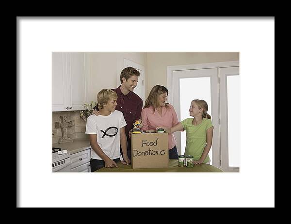 Child Framed Print featuring the photograph Family putting canned food in donations box indoors by Jupiterimages