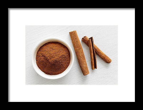Heap Framed Print featuring the photograph Finely ground cinnamon in white ceramic bowl isolated on white wood background from above. Cinnamon sticks. by Etienne Voss